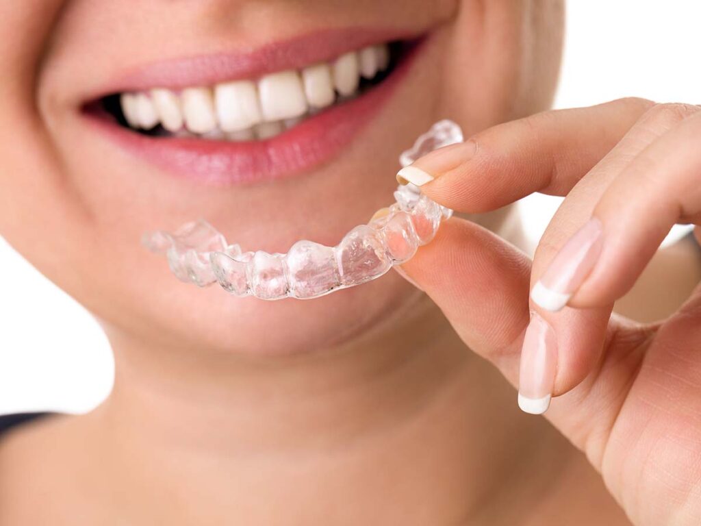 Smiling female holding invisible teeth braces front of perfect smile 