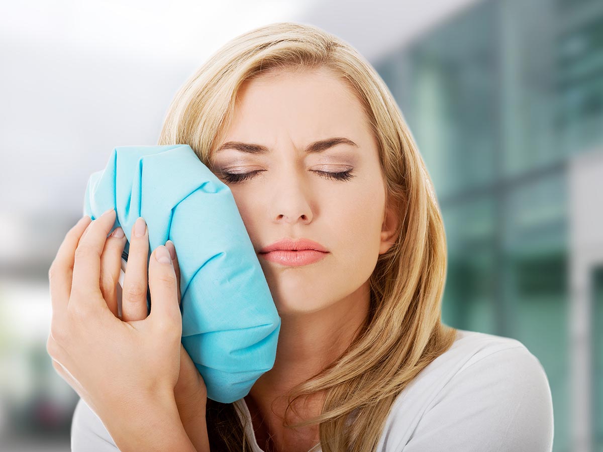 Woman holding ice pack agains her jaw and face