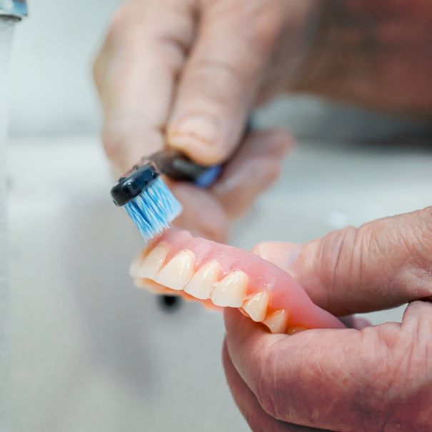 Elderly person using a toothbrush to clean dentures