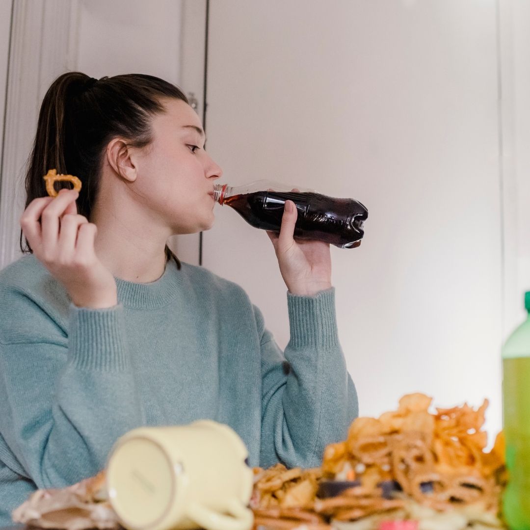 woman drinking soda and eating junk food